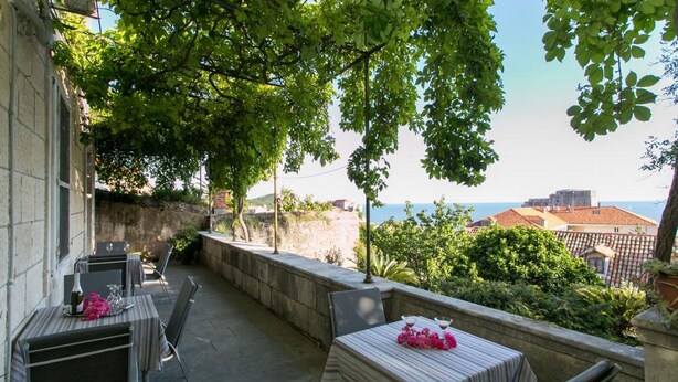 An outdoor patio with tables and chairs, overlooking a coastal area with buildings and greenery.