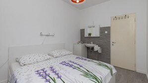A bedroom with a bed, a bedside table, a mirror, a sink, and a door.