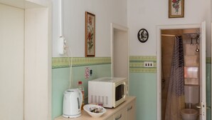 A compact kitchen with a microwave, kettle, and a bowl on the counter.