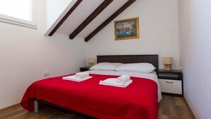 A bedroom with a red bedspread, two white pillows, a wooden headboard, a nightstand with a lamp, and a painting on the wall.