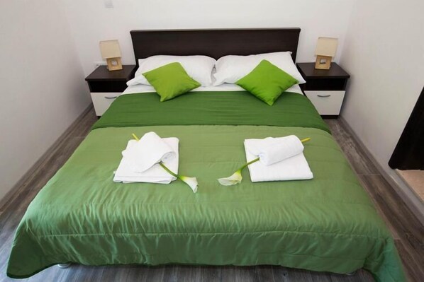 Una cama bien hecha con ropa de cama verde, almohadas blancas y un cabecero verde. Hay dos mesitas de noche con lámparas y una pequeña caja de madera en cada una.