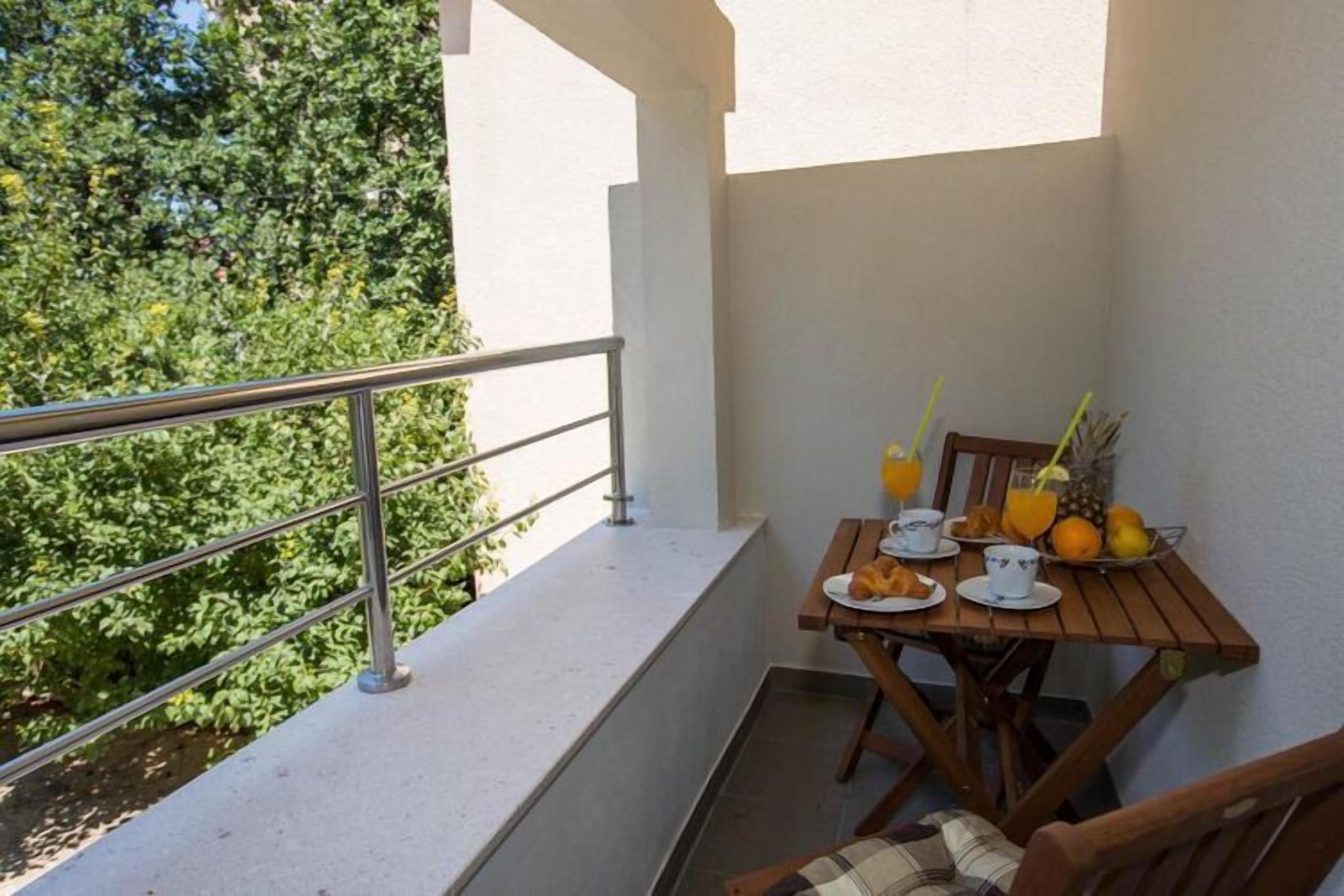 En balkon med et bord dækket til morgenmad, blandt andet croissanter, appelsinjuice og frugt.