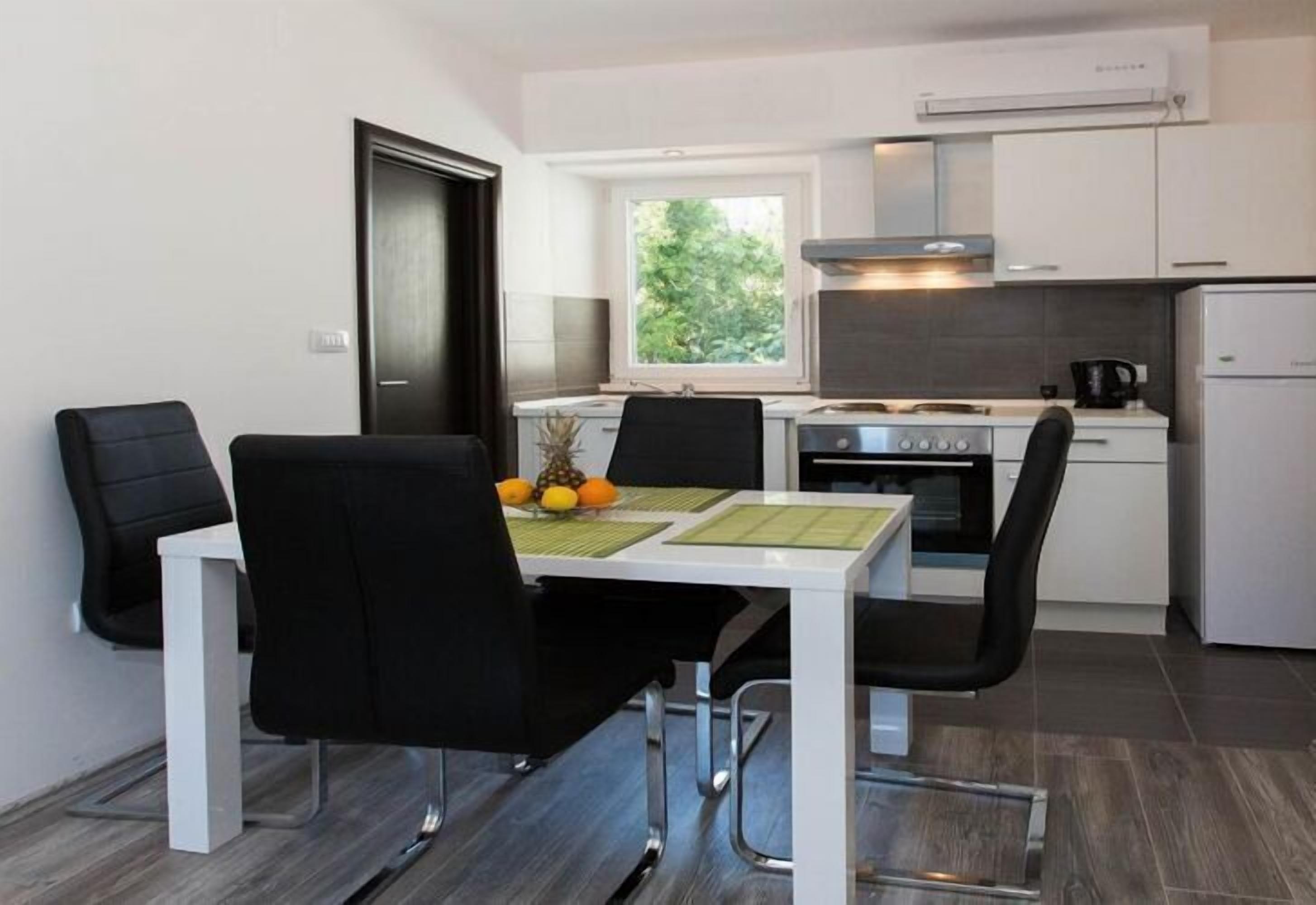A compact kitchen with a dining area, featuring a white table, black chairs, and a window providing natural light.