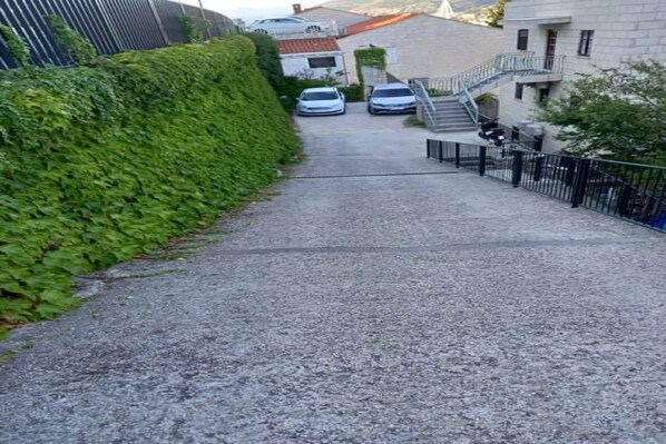 A narrow gravel path leading to a building with a staircase and a car parked nearby.