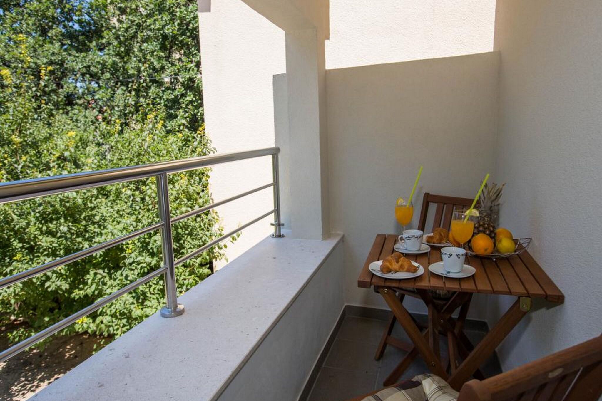 Un balcón con una mesa dispuesta para el desayuno, incluyendo cruasanes, zumo de naranja y fruta.
