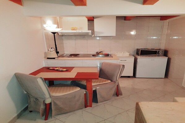 A compact kitchen with a dining table, chairs, a microwave, a small refrigerator, and a sink.