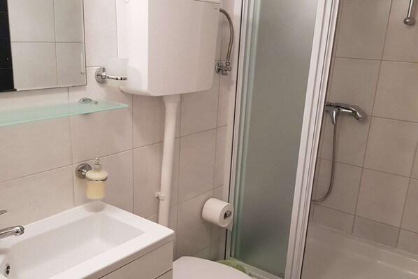 Casa de banho com lavatório branco, sanita e cabine de duche em vidro.