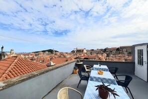A rooftop terrace with a table set for dining, overlooking a cityscape with red-tiled roofs.