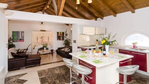 Una cocina moderna con una isla central, taburetes de bar y un área de comedor con sofá y mesa de centro.