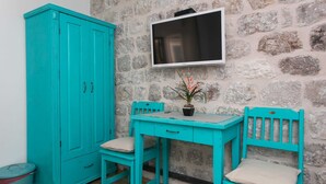 Un gabinete turquesa, un televisor montado en una pared de piedra, y una pequeña mesa con sillas.