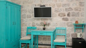 Habitación con muebles turquesa, pared de piedra, televisor de pantalla plana, una mesita con una planta y un hervidor sobre un mueble.