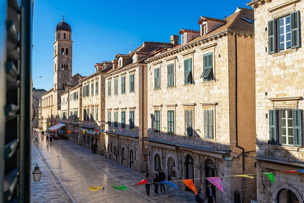 A historic street with stone buildings, a prominent tower, and colorful flags.
