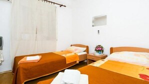 A hotel room with two single beds, each with a brown bedspread and a white towel folded on the bed. There is a small bedside table with a lamp and a vase with flowers.
