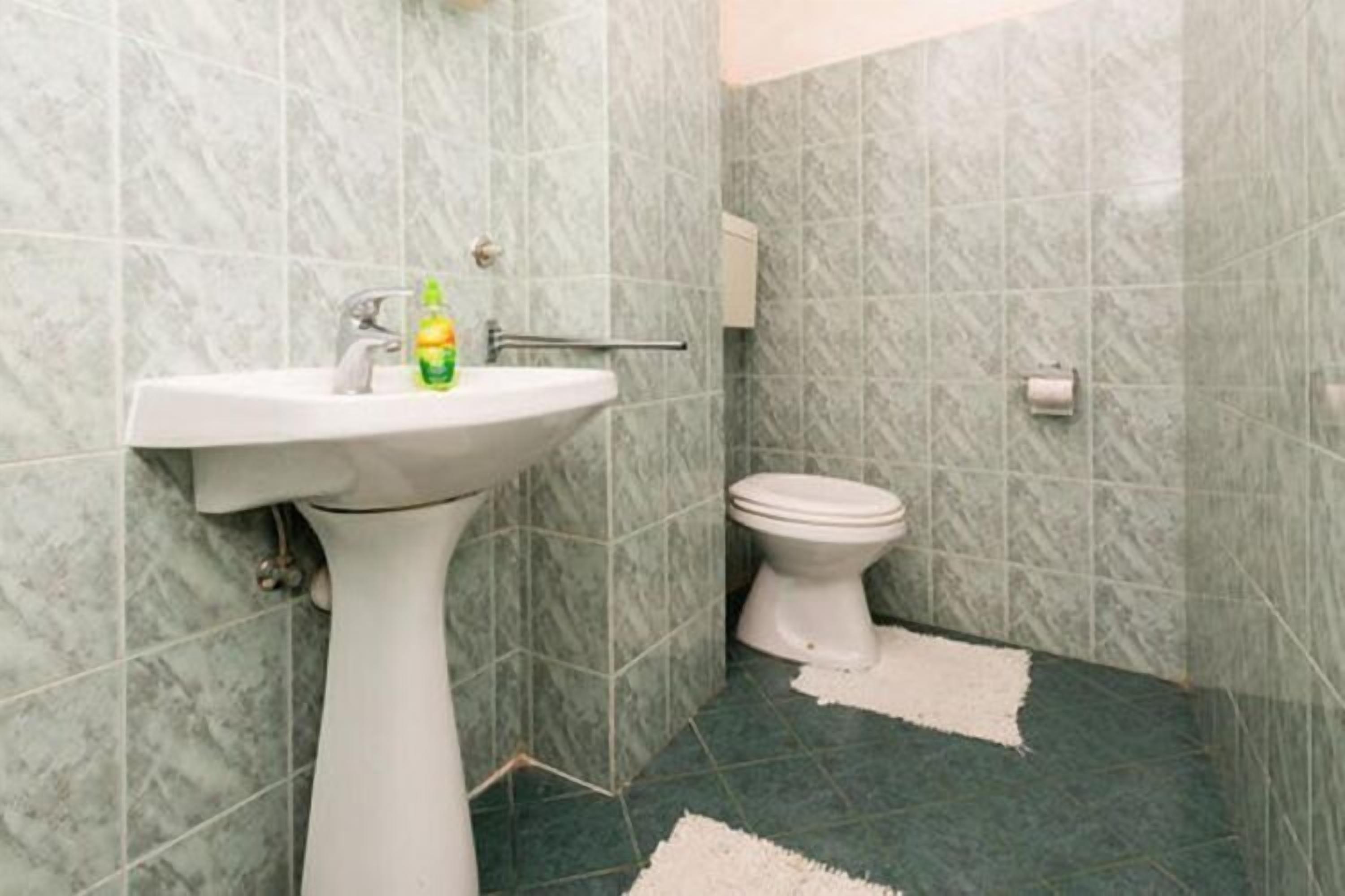 A bathroom with a pedestal sink, toilet, and green marble tiles.