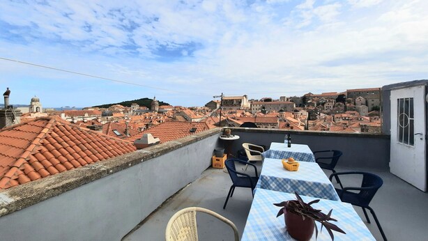 A rooftop terrace with a table set for dining, overlooking a cityscape with red-tiled roofs.