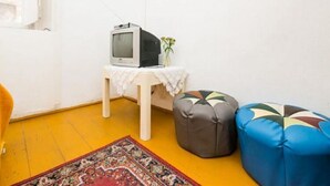 A small room with a television on a table, two colorful ottomans, a patterned rug, and a yellow floor.