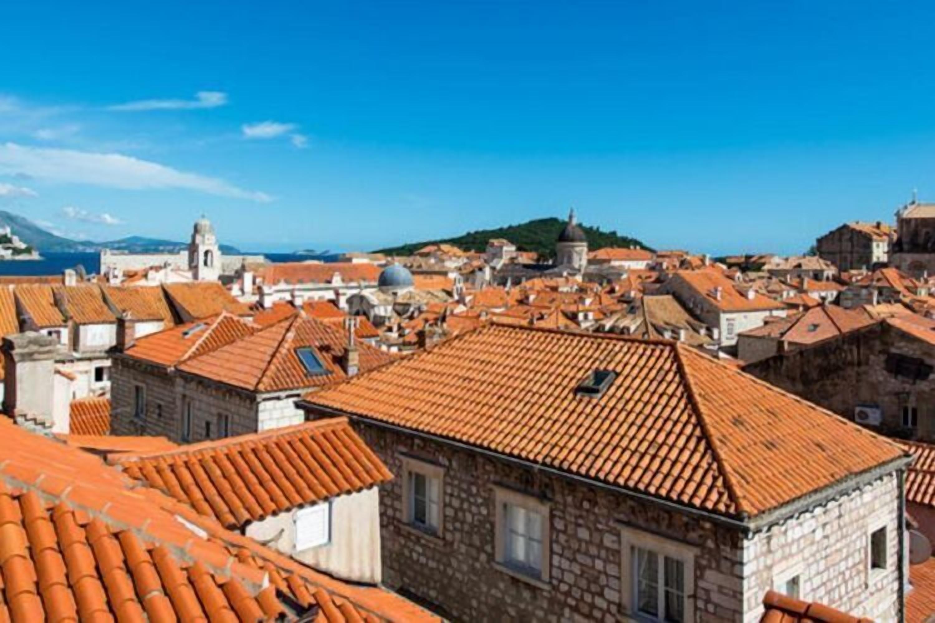 Une ville historique, avec des bâtiments aux toits de tuiles rouges, une église imposante et une colline en arrière-plan.
