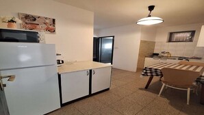 A compact kitchen with a refrigerator, a microwave, a table with a checkered tablecloth, and a hanging light fixture.