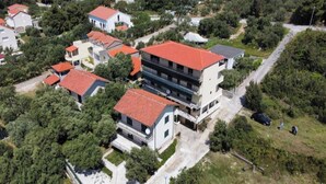 An aerial view of a residential area with multiple houses, some with red roofs, surrounded by greenery.