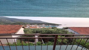 A balcony with a view of a coastal town, a clear sky, and a distant mountain range.