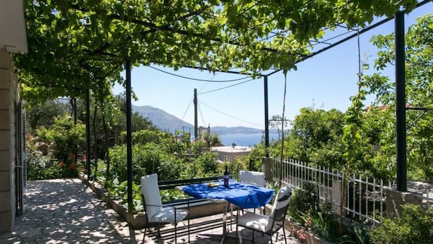 Un patio exterior con mesa y sillas, rodeado de vegetación y vistas al mar y a las montañas.