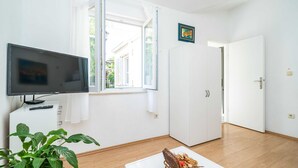 A room with a TV, a window, a door, and a plant.