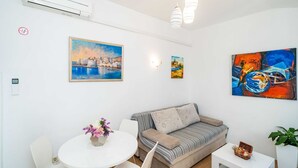 A modern living room with a sofa, a dining table with chairs, and artwork on the walls.