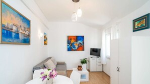 A modern living room with a sofa, a dining table with flowers, a TV, and artwork on the walls.