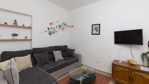 A living room with a grey sofa, a glass coffee table, a wooden cabinet, and a flat-screen TV.