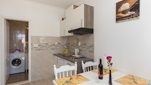 A compact kitchen with a washing machine, a dining table with chairs, and a painting on the wall.