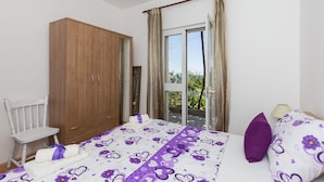A bedroom with a bed, a wooden wardrobe, a chair, and a balcony with curtains.