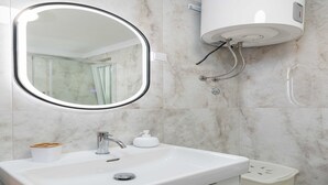 A bathroom with a white sink, a mirror, a handheld showerhead, and a toilet.