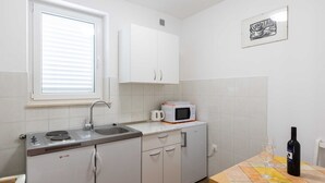 A compact kitchen with white cabinets, a microwave, a sink, and a table with a bottle and glass.