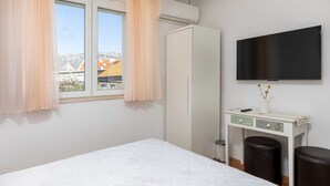 A bedroom with a bed, a wardrobe, a desk with a TV, and a window with curtains.