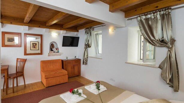 A cozy room with a wooden ceiling, a sofa, a TV, and a window with curtains. - Apartments Ivana Old Town -Superior Studio - APT2 (Dubrovnik)