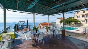 A covered outdoor area with tables and chairs, a pool, and a view of the sea. - Apartments Klis -Studio Apartment with Terrace - 2 (A) (Soline)