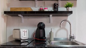 A kitchen with a black countertop, a coffee maker, a toaster, a sink, and a shelf with jars and a plant. - Apartments Ivana Old Town - Standard Studio - APT3 (Dubrovnik)
