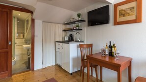 A compact kitchen with a sink, a small countertop, and a dining area with a table and chairs. There is a television mounted on the wall and a framed picture above the counter. - Apartments Ivana Old Town - Standard Studio - APT3 (Dubrovnik)