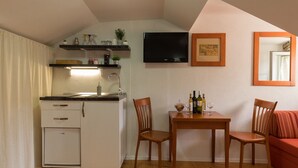 A compact kitchen with a built-in refrigerator, a dining table with two chairs, a TV mounted on the wall, and a small seating area with a sofa. - Apartments Ivana Old Town - Standard Studio - APT3 (Dubrovnik)