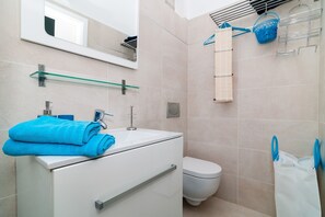 A modern bathroom with a glass shelf above the sink, a white toilet, and a towel rack with a blue towel.