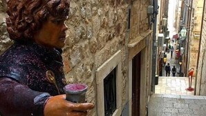 Una calle estrecha con una estatua de un hombre sosteniendo una bebida.