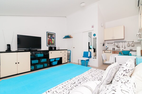 A modern bedroom with a large bed, a TV, a desk, and a kitchenette.