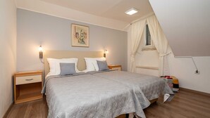 A bedroom with a bed, two bedside tables, a nightstand, a window with curtains, and a painting on the wall.