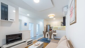 Una sala de estar moderna con un televisor de pantalla plana, un sofá, una mesa de centro y una zona de comedor con sillas.