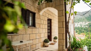 Un bâtiment en pierre doté d’un patio carrelé, d’une table blanche et de deux plantes en pot.