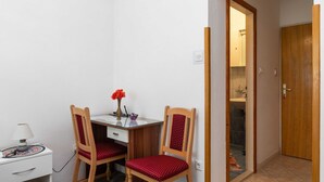 A small room with a desk, two chairs, a lamp, and a vase with flowers.
