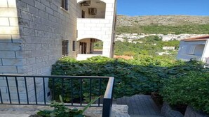 A building with a stone facade, a balcony, and a view of a hillside town. - Guest House Cesic - Double Room No4 (Dubrovnik)