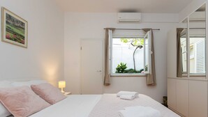 A bedroom with a bed, pillows, a window with curtains, a bedside lamp, and a wall-mounted air conditioner. - Rooms Batina- Standard Double Room-2 (Dubrovnik)