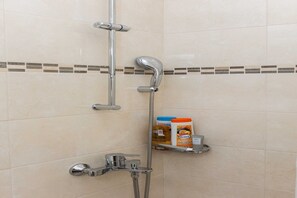 A shower with a chrome faucet, a handheld showerhead, and a shelf with toiletries.