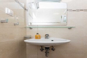 A bathroom with a white sink, a mirror, and a glass shelf.